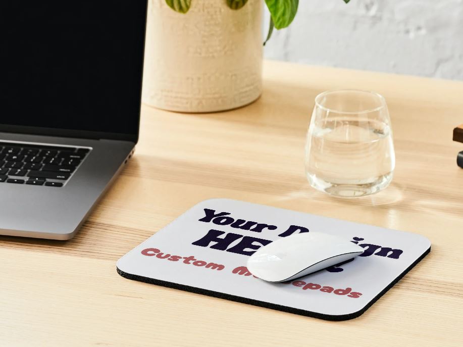 Custom mouse pad on a desk with a laptop and glass in the background